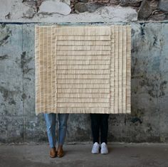 two people standing next to each other holding up a piece of fabric on the wall