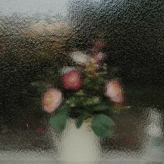 a vase filled with pink flowers sitting on top of a window sill covered in rain