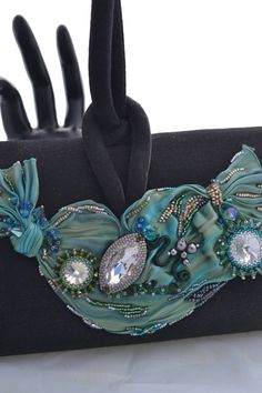 Beautifully beaded and embellished Shibori Ribbon accents this little black evening bag with shades of seafoam green, turquoise blue and forest green. Its covered with Swarovski crystals in various sizes and shapes, and its embellished on both sides! Hand beaded by me in my Las Vegas studio, this striking evening bag measures approximately 7 inches wide, almost 4 1/2 inches tall, and about 2 inches wide, just big enough to tuck in your cell phone, mad money, and a lipstick or two, for that great Luxury Turquoise Evening Bag, Luxury Green Beaded Bags, Elegant Turquoise Bag For Formal Occasions, Elegant Green Evening Bag, Green Beaded Evening Bag, Elegant Green Beaded Evening Bag, Shibori Ribbon, Mad Money, Embroidered Purse