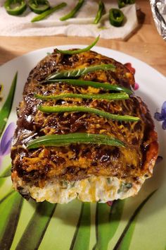 a piece of meat covered in sauce and green beans on a white plate with purple flowers