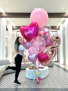 a woman standing next to a large bunch of heart shaped balloons in a lobby area