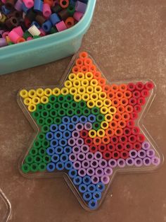 a star shaped object made out of colored beads next to a plastic container filled with colorful crayons