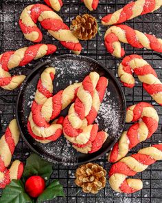 christmas cookies with red and white icing on a cooling rack next to pine cones