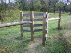 a wooden fence in the middle of a grassy field with trees and bushes behind it