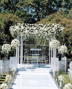 an outdoor ceremony setup with white flowers and greenery on either side of the aisle