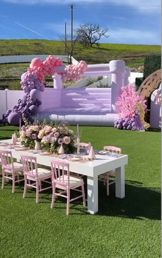 a table set up with pink chairs and flowers on it in front of a white fence