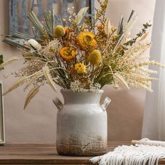 a white vase filled with lots of flowers on top of a wooden table next to a window