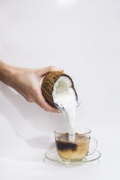 a person pouring milk into a glass cup with a coconut in it and on the side