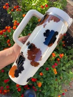 a person holding a coffee cup with brown and black spots on it in front of some flowers