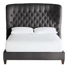 an upholstered bed with white sheets and pillows