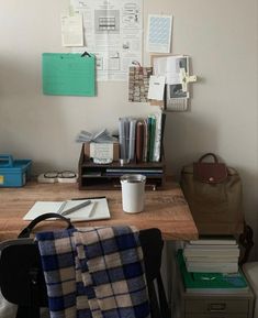 a wooden desk topped with a laptop computer next to a pile of books and papers