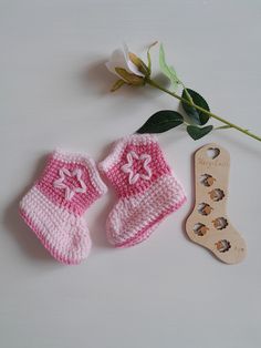 two crocheted baby booties next to a wooden spoon and flower on a white surface