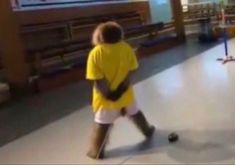 a young boy in yellow shirt and white shorts playing with a black ball on the floor