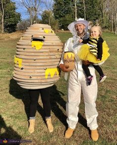 a man and woman in bee costumes holding a child next to a giant honey pot