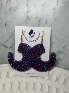 the purple glitter mustache earrings are on display in front of a white card and marble background