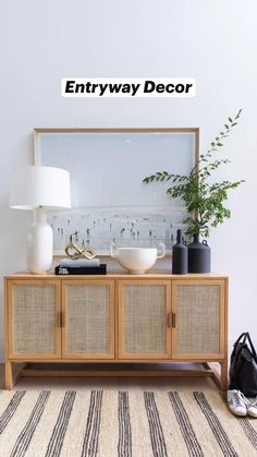 a sideboard with two bowls and a plant on it in front of a white wall