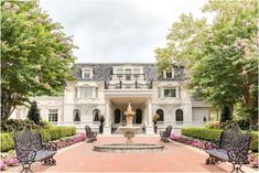 a large white house with a fountain in front of it and lots of flowers on the ground