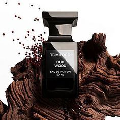 a bottle of tom ford oud wood cologne on a wooden branch with red berries