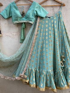 A three-piece ocean green ruffle lehenga set from the Priti Sahni collection. This elegant ocean green butti georgette lehenga with big ruffle detailing and gota border is paired with an ocean green raw silk blouse with sequin, pearl border. The lehenga has side hanging ball tassels to the waistline. And the blouse has a coin-beads tassel tie-up at the back. The outfit is completed with an ocean green sequined butti work dupatta with scalloped edging. Haldi Dress Ideas, Lehenga Green, Ruffle Lehenga, Pearl Border, Haldi Dress, Brocade Lehenga, Raw Silk Blouse, Simple Lehenga, Indian Wedding Fashion