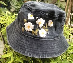 a gray hat with white flowers on it sitting in front of some bushes and plants