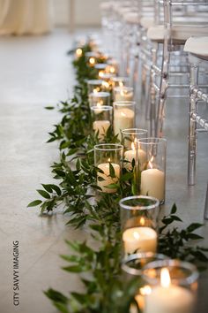 rows of candles lined up on the floor in front of white chairs with greenery