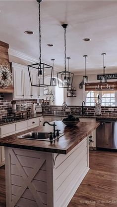 a kitchen with white cabinets and wooden counter tops, an island in the middle is surrounded by hanging lights