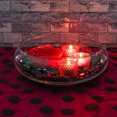 a bowl filled with candles sitting on top of a red table cloth next to a brick wall