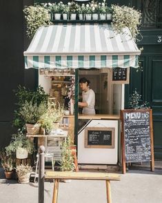 there is a man standing at the counter in front of this small shop that sells plants