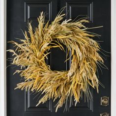 a black door with a wreath on it and some yellow grass in front of it