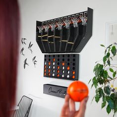 a woman is holding an orange in front of a wall with several birds on it