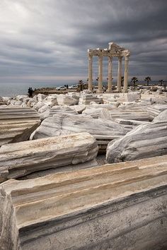 some very large rocks by the ocean under a cloudy sky with an old building in the background