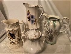 four different vases are sitting on a white tablecloth, one is empty and the other has flowers painted on it