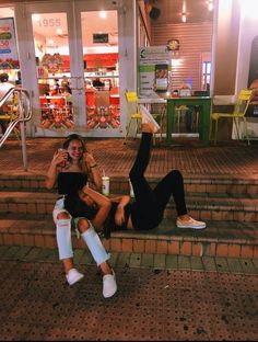 two young women sitting on the steps in front of a store with their feet up