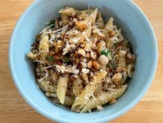 a blue bowl filled with pasta and meat on top of a wooden table next to a fork