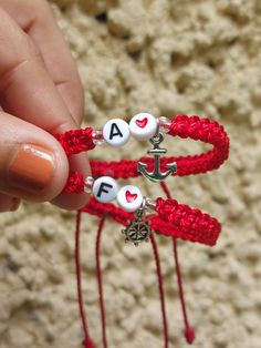 someone is holding two red bracelets with hearts and an anchor on them, one for each