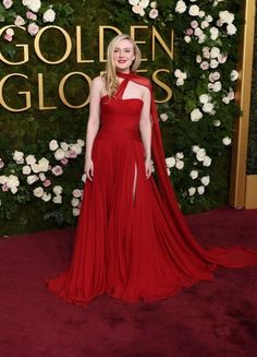 a woman in a red gown standing on a red carpet with white flowers behind her