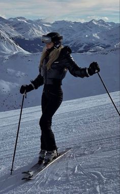 a woman riding skis down the side of a snow covered slope with mountains in the background