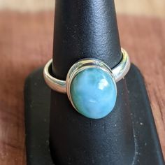 a ring that is sitting on top of a black piece of wood with a blue stone in the middle