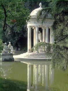 a pond with statues and trees surrounding it