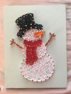 a snowman made out of string and beads on top of a piece of paper