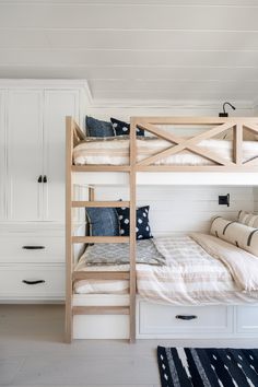 a bunk bed in a bedroom with white walls and wooden furniture on the bottom level