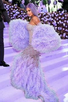 a woman in a purple feathered dress standing on the steps with her arms outstretched