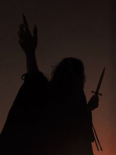 the silhouette of a person holding two knives in front of an orange sky at night