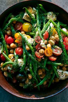 a bowl filled with green beans, tomatoes and chickpeas on top of a table