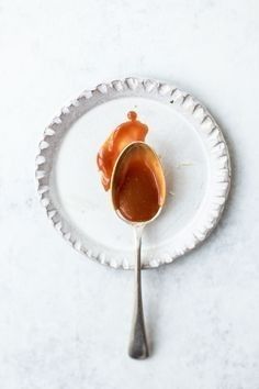 a spoon with peanut butter on it sitting on a white plate next to another spoon