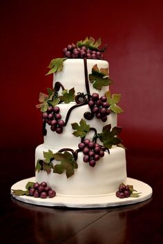 a three tiered white cake with grapes on the top and green leaves around it