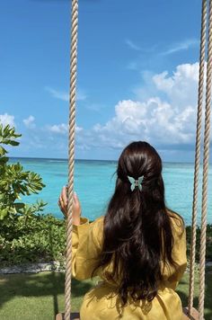 a woman sitting on a swing looking out at the ocean