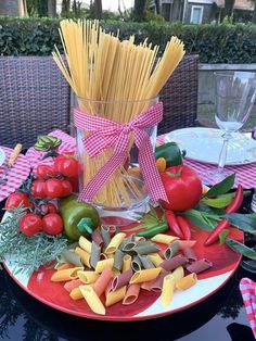 a plate with pasta, tomatoes and other vegetables on it next to a glass vase