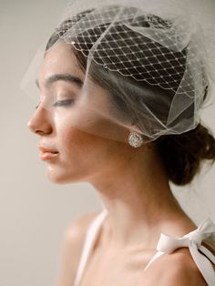 a woman with a veil on her head wearing a white dress and diamond earring