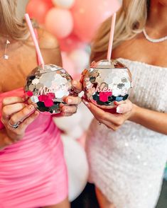 two women in dresses holding up some disco ball shaped ornaments with the word bride on them